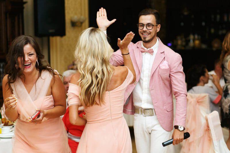 Drei festlich gekleidete Personen in Rosa lachen und klatschen freudig ab