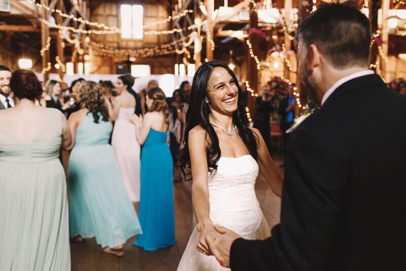 Eine lachende Braut im weißen Kleid tanzt mit einem Mann auf einer festlichen Hochzeit