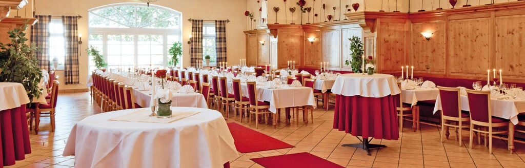 Eleganter Festsaal mit roten Tischdecken, weißen Stühlen und Kerzenlicht