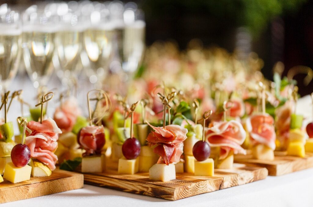 Das Buffet bei der Rezeption. Gläser mit Wein und Champagner. Auswahl an Canapés auf einem Holzbretter. Bankettservice. Catering-Speisen, Snacks mit Käse, Jamón, Prosciutto und Obst.
