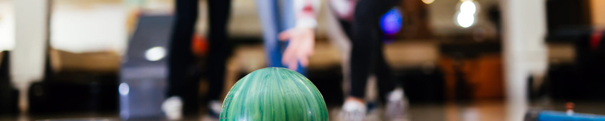 Zwei Personen in sportlicher Kleidung konzentrieren sich auf eine grüne Bowlingkugel