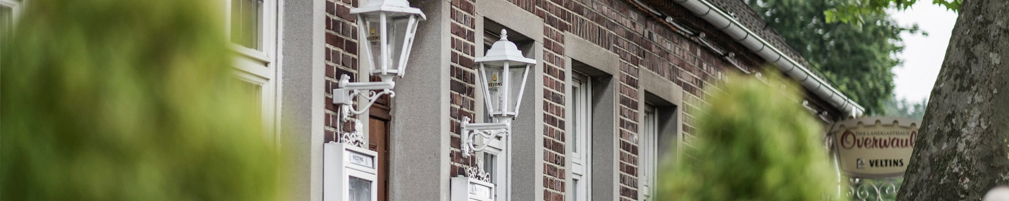 Ein rotes Backsteingebäude mit weißen Laternen und grünen Bäumen davor