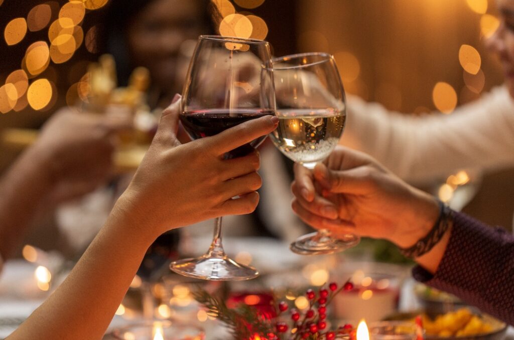 Nahaufnahme von Händen, die bei einer Weihnachtsfeier mit Wein anstoßen