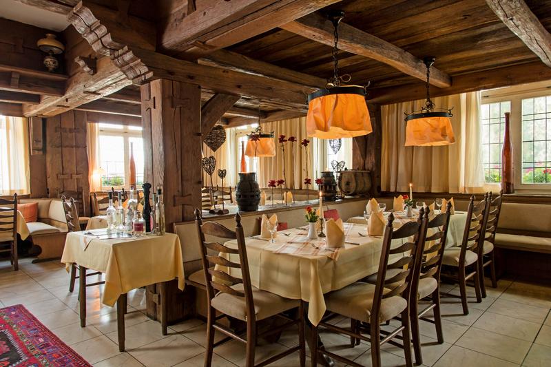 Gemütliches rustikales Restaurant mit Holzbalkendecke, gelben Vorhängen und gedeckten Tischen