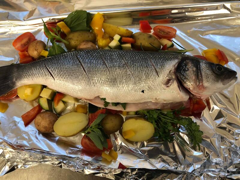 Ein ganzer frischer Fisch liegt auf buntem Gemüse in Alufolie vorbereitet zum Garen